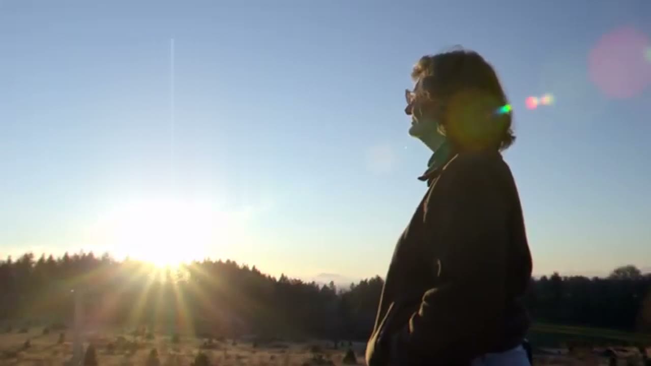 Dr. Elaine Ingham in silhouette on a hilltop, looking toward a rising sun.